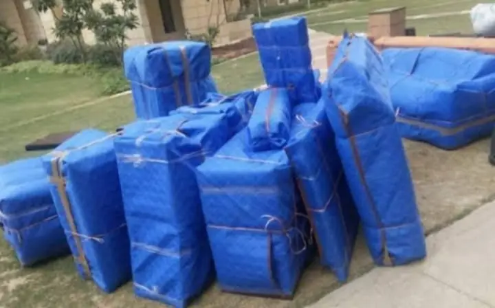 Furniture and cartons wrapped in blue sheets on a lawn