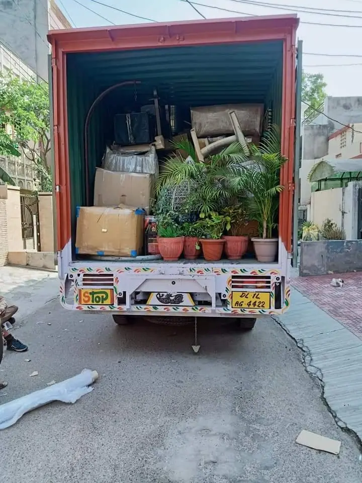 The open back of a truck loaded with furniture, cartons and potted plants